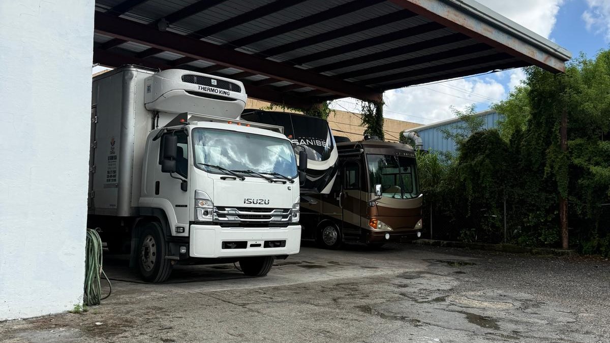 A box truck and an RV under a covered outdoor bay at Tour America RV's in Doral